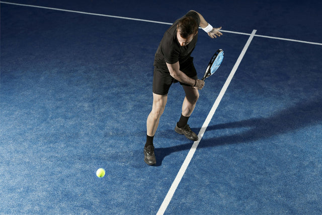 Joueur de padel en position basse prêt à défendre une balle