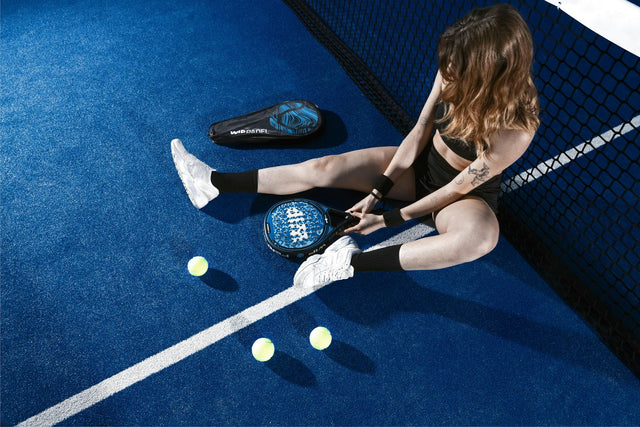 Joueuse de padel assise sur un court bleu avec sa raquette, sa housse et des balles