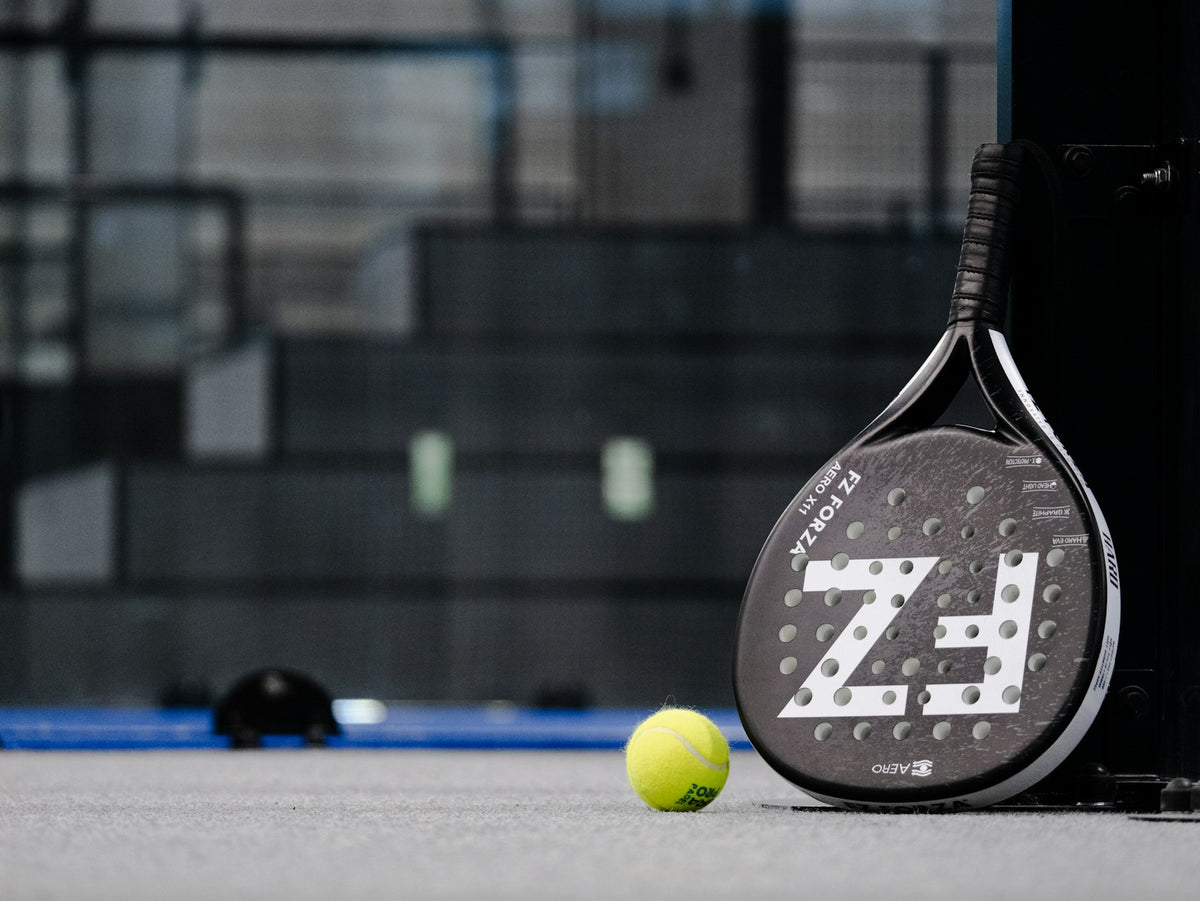 Raquette de padel posée debout à côté d'une balle jaune sur un court