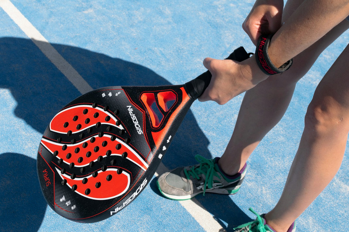 Joueur tenant une raquette de padel rouge et noire sur un court bleu