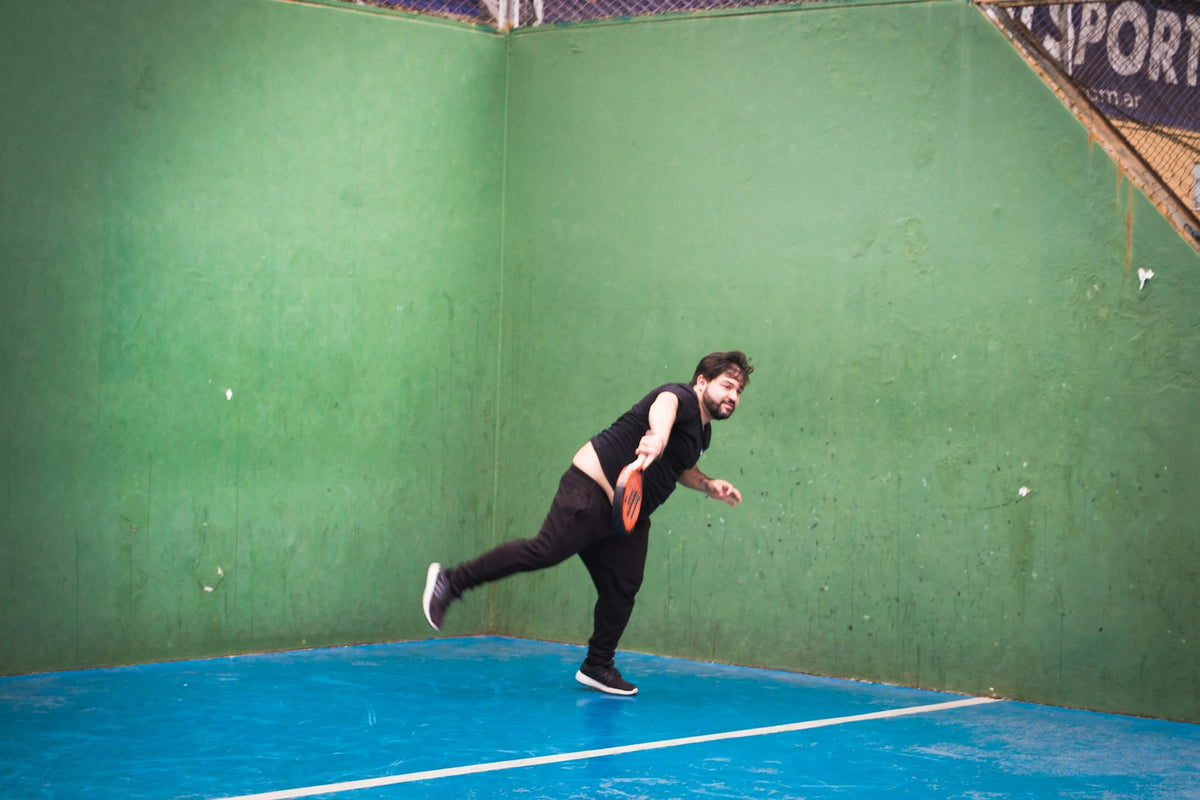 Joueur de padel débutant frappant la balle devant un mur vert
